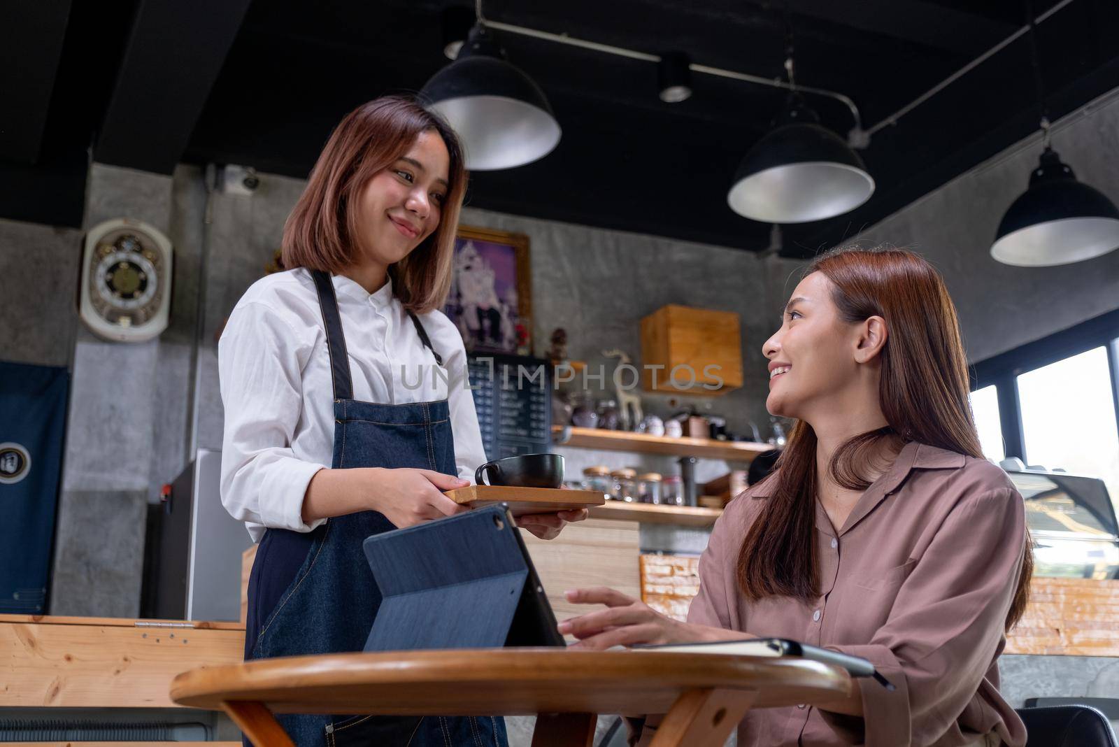 Beautiful working woman sit in coffee shop and get service from barista woman and they smile to each other with happy emotion.