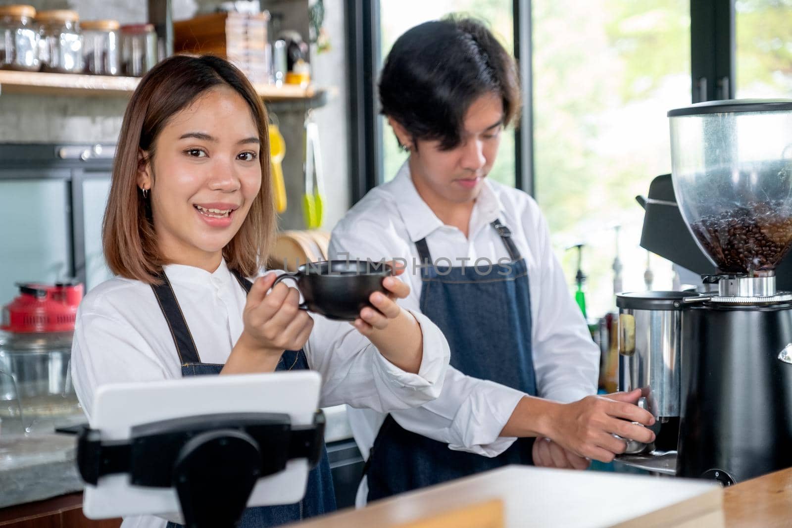 Barista woman or coffee maker hold and present a cup of coffee to camera with smiling. Concept of happy working with small business and sustainable.