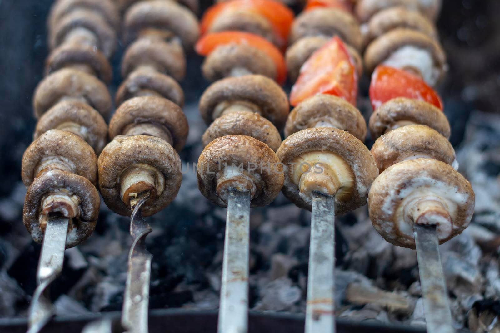 Mushrooms on skewers roast on coals. Barbeque. In nature, on the grill, mushrooms in combination with tomatoes. by Essffes