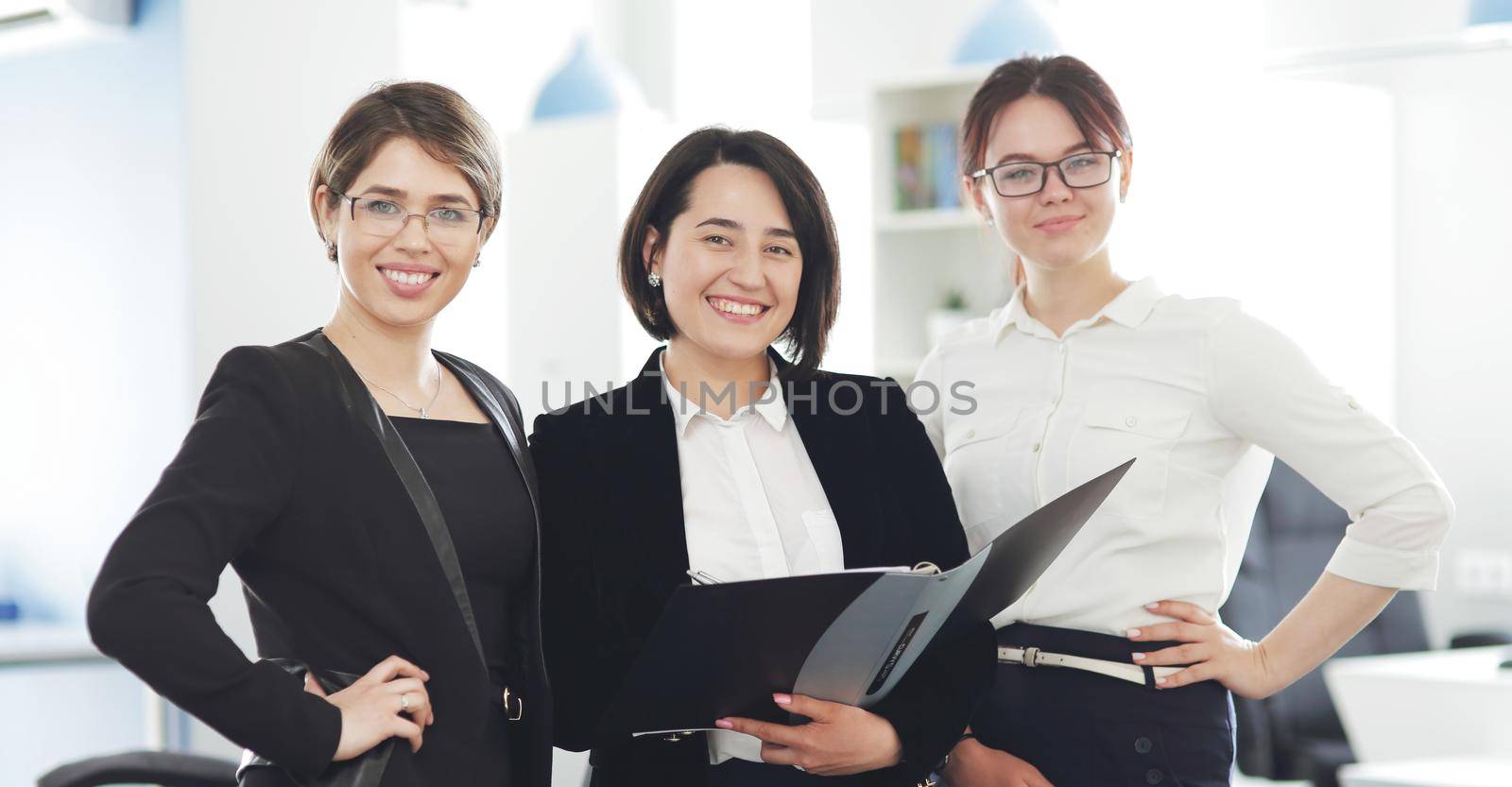 Three young successful business women in the office smiling happily. 