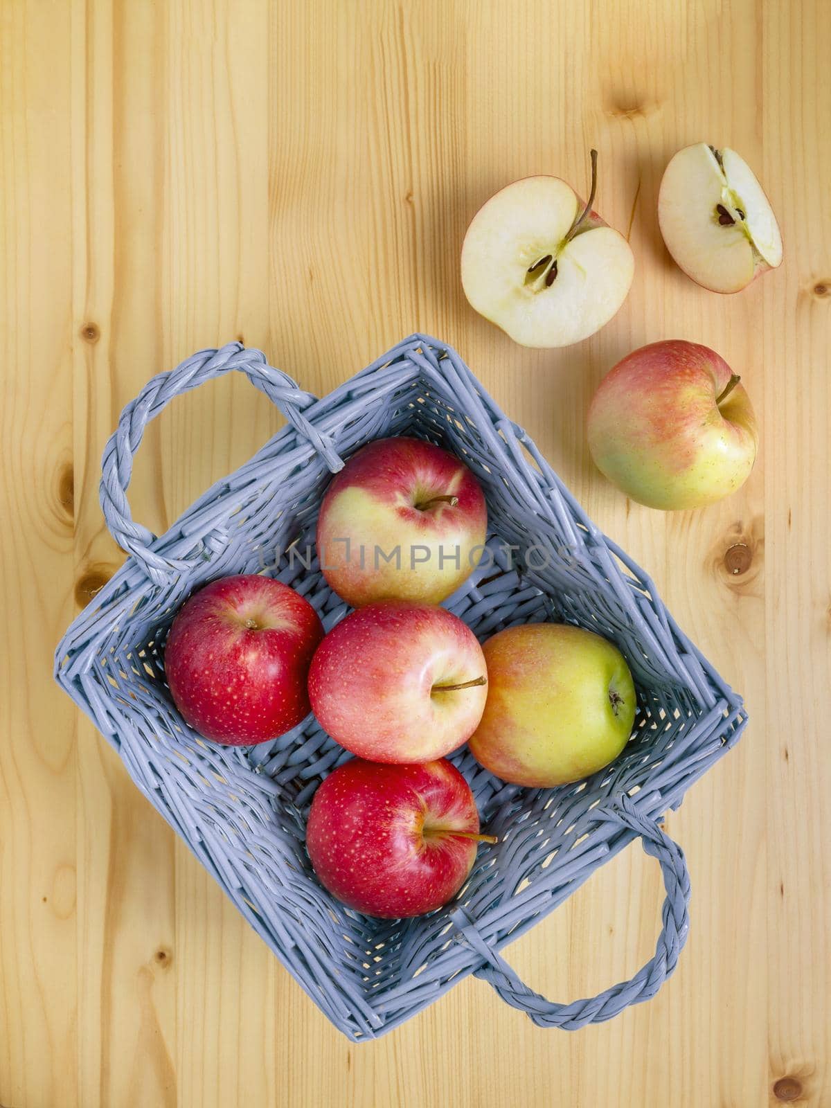 Ripe red and yellow apples in a basket on a bright wooden background. Some out of the bin. Top view.