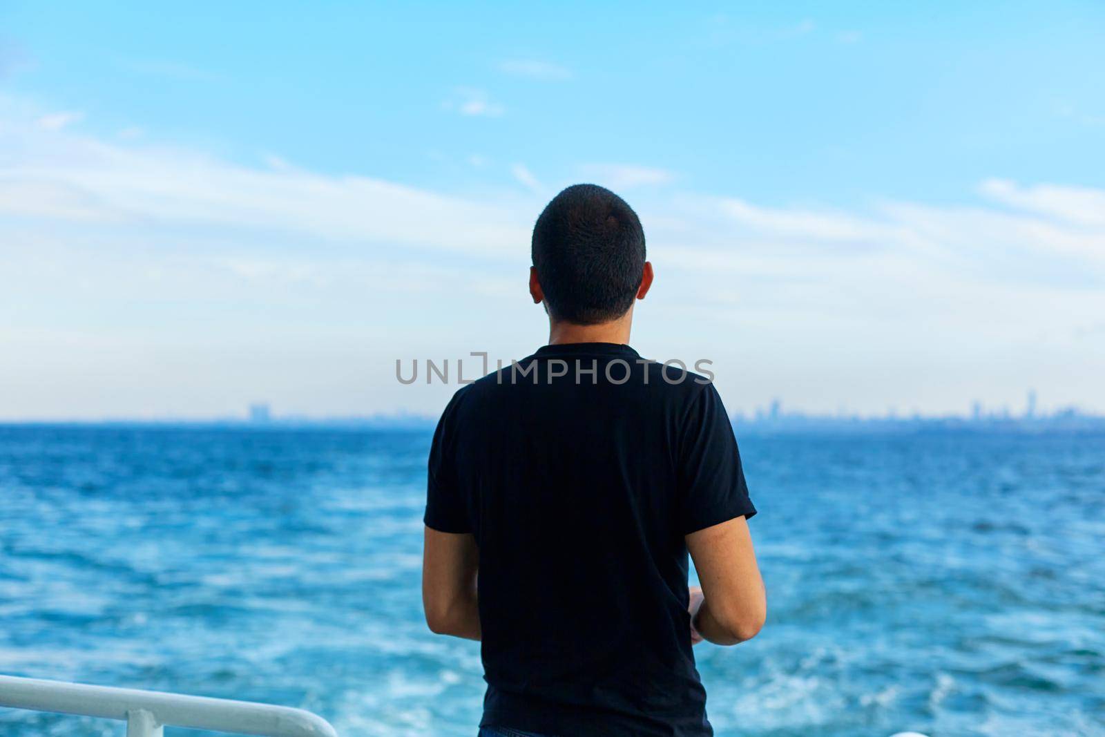 The guy throws bread to the seagulls flying over the ferry.