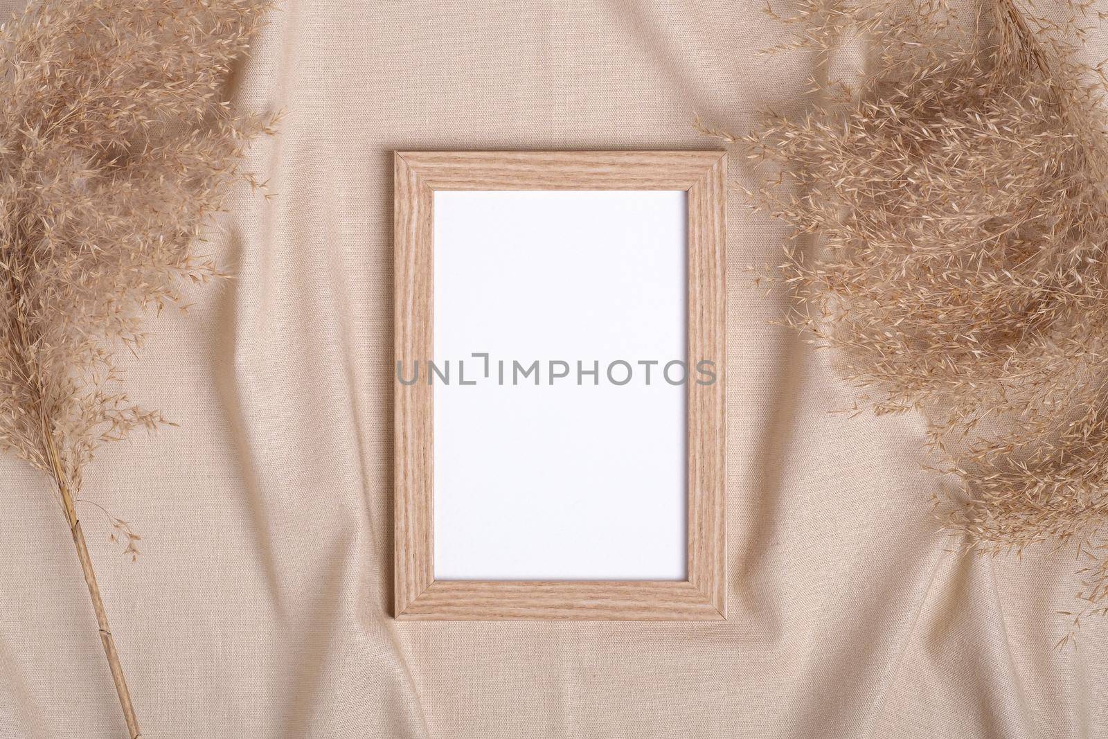 Picture frame with blank paper card mockup near to pampas dry grass on beige neutral colored textile