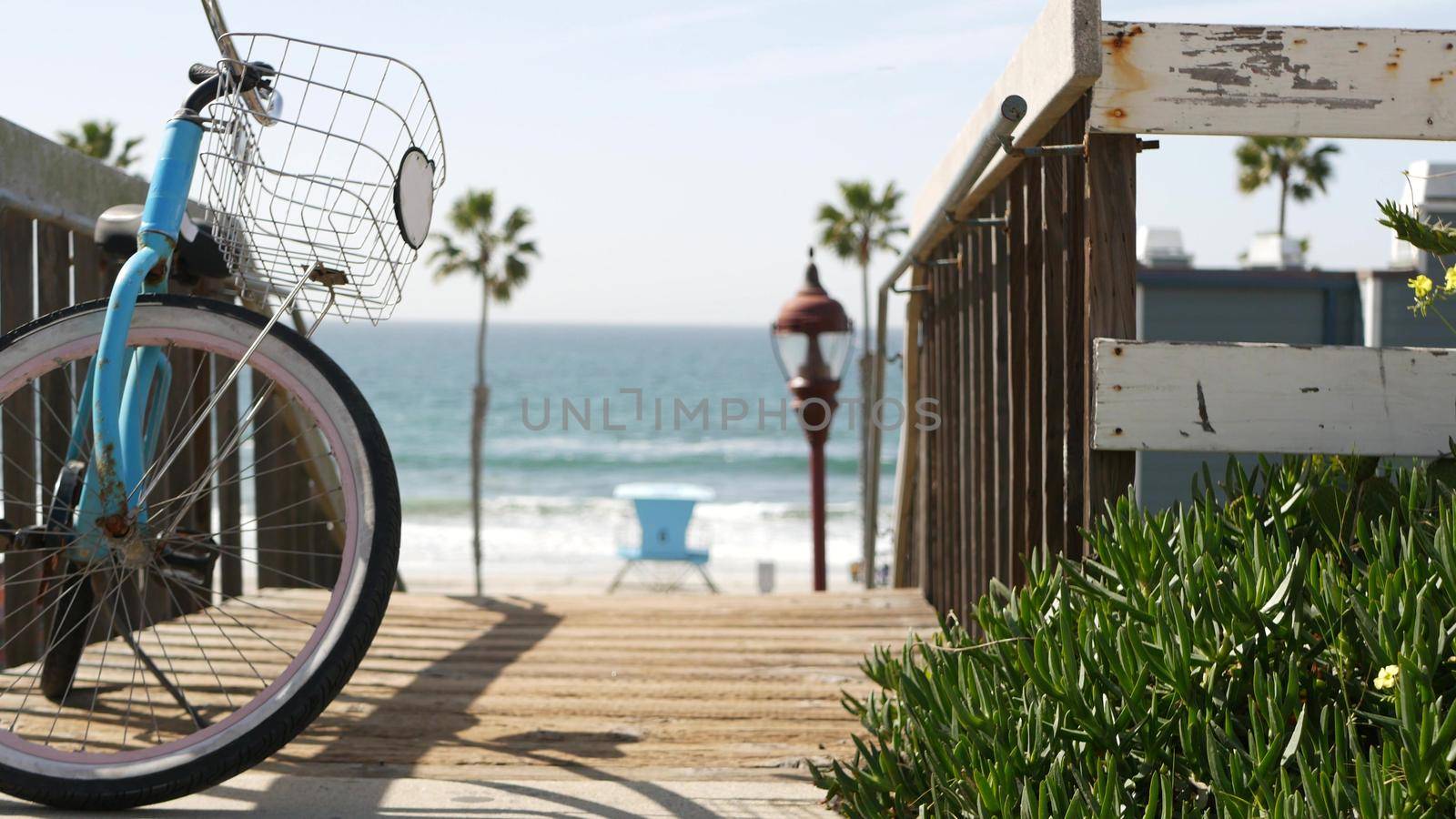 Blue bicycle, cruiser bike by ocean beach, pacific coast, Oceanside California USA. Summertime vacations sea shore. Vintage cycle by wooden stairs, stairway or staircase. Tropical palms and lifeguard