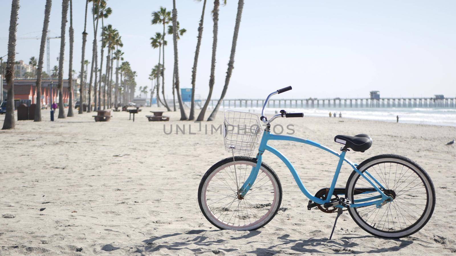Blue bicycle, cruiser bike by sandy ocean beach, pacific coast near Oceanside pier, California USA. Summertime vacations, sea shore. Vintage cycle, tropical palm trees, lifeguard tower watchtower hut