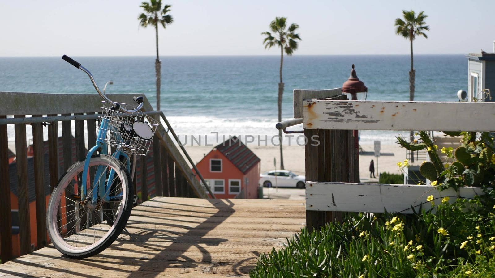 Blue bicycle, cruiser bike by ocean beach, pacific coast, Oceanside California USA. Summertime vacations on sea shore. Vintage cycle near wooden stairs, stairway access. Staircase, tropical palm trees