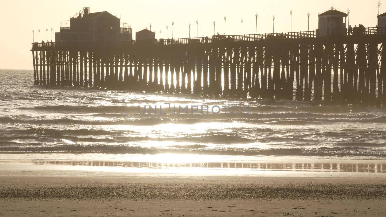 Wooden pier on piles, silhouette at sunset, California USA, Oceanside. Waterfront resort, pacific ocean tide, tropical beach. Summertime coastline vacations atmosphere. Sunny sea waves at sundown.