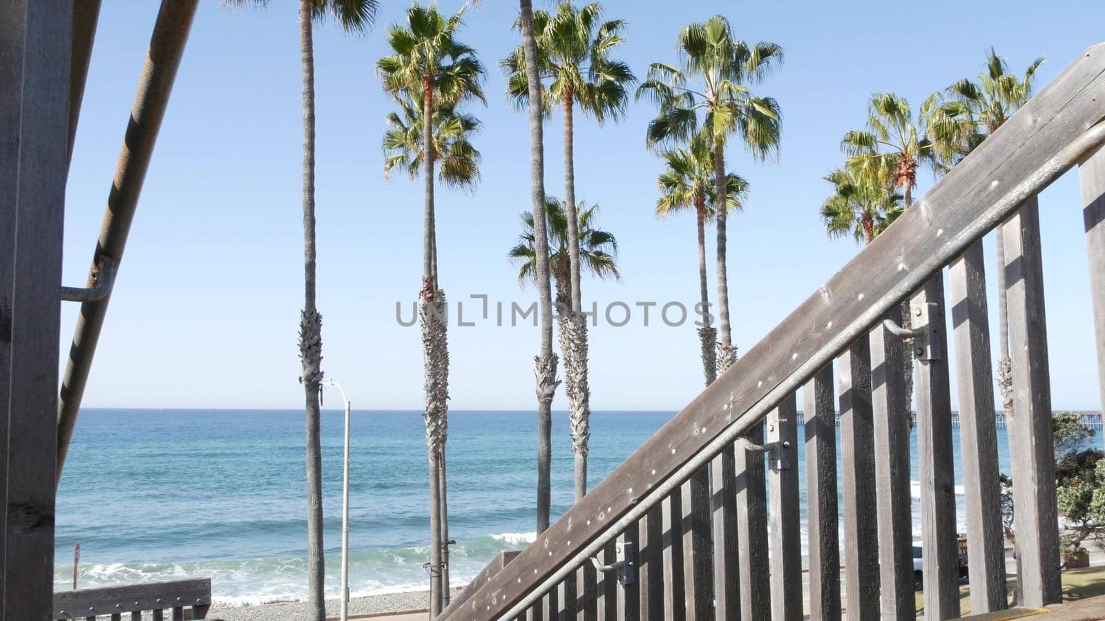 Wooden stairs, beach access in Oceanside, California USA. Coastal stairway, pacific ocean waves and palm trees. Vacations by sea in United States. Sunny tropical day, summertime aesthetic. Staircase.