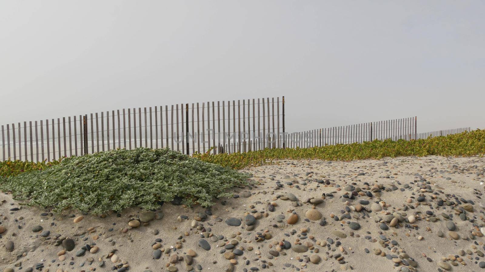 Wooden picket fence, sandy misty beach, Encinitas California USA. Pacific ocean coast, dense fog on empty sea shore. Coastline near Los Angeles, boards in milky smog haze. Gloomy weather on shoreline.
