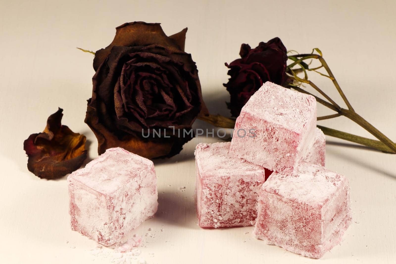 Cubes of Turkish delight sweets with old red roses on white