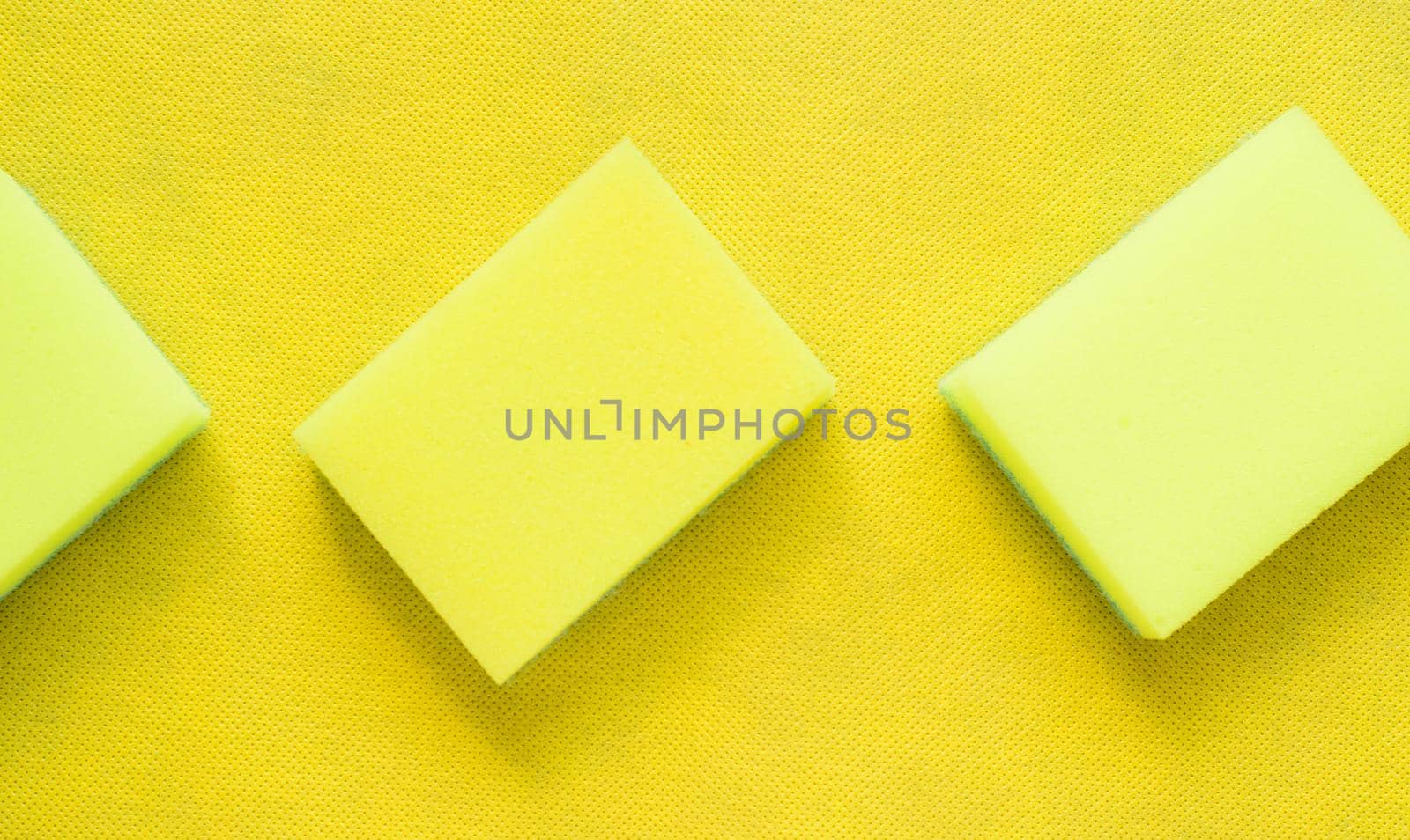 several bright yellow dishwashing sponges on a yellow background.