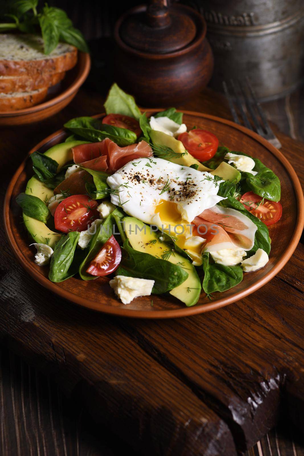 Eggs Benedict (Poached) with Parma ham, slices of avocado, tomato and tender spinach leaves, seasoned with flavored spicy olive oil