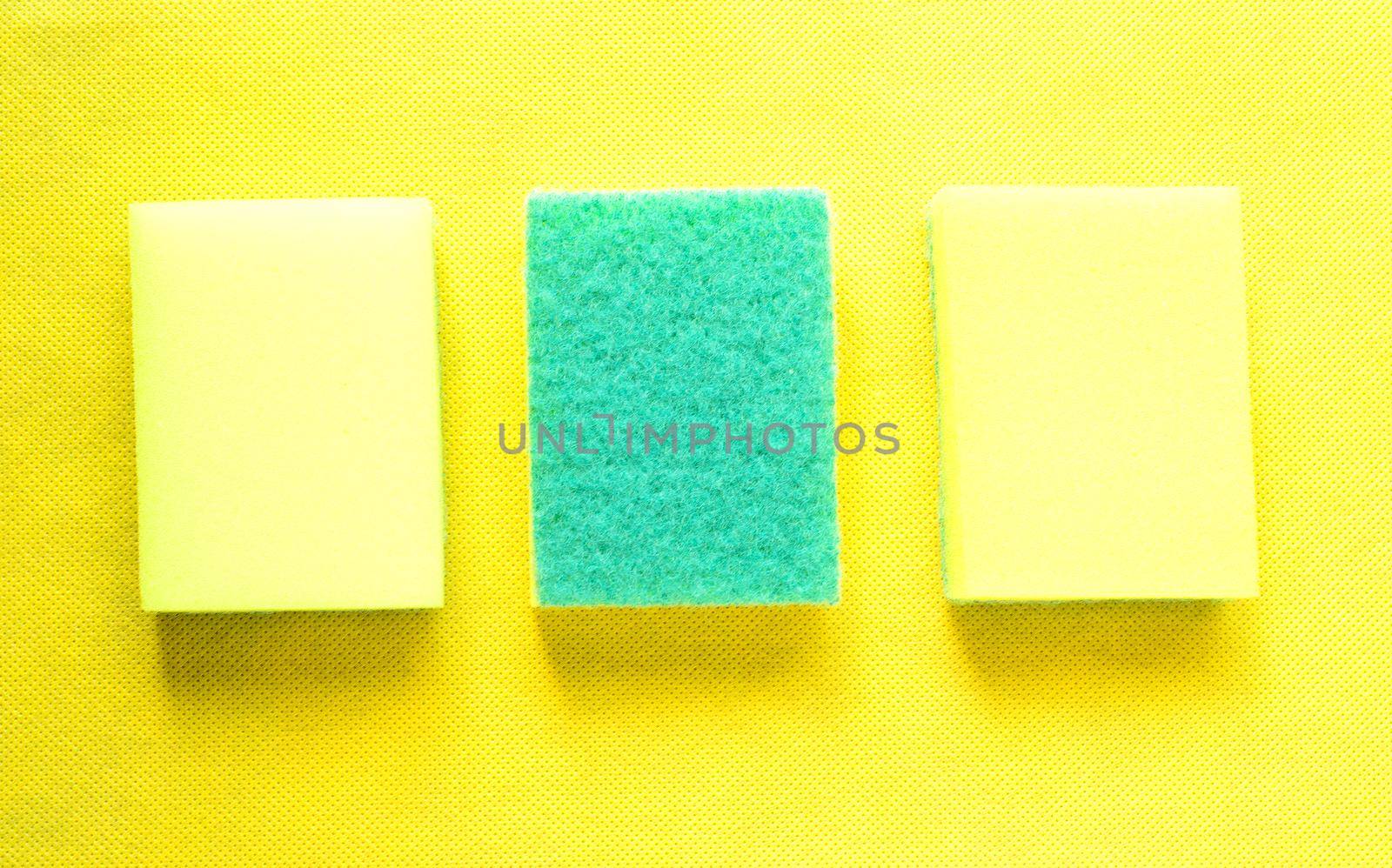 Two bright yellow sponges for cleaning surfaces and one upside-down to remove stubborn dirt on a yellow background.