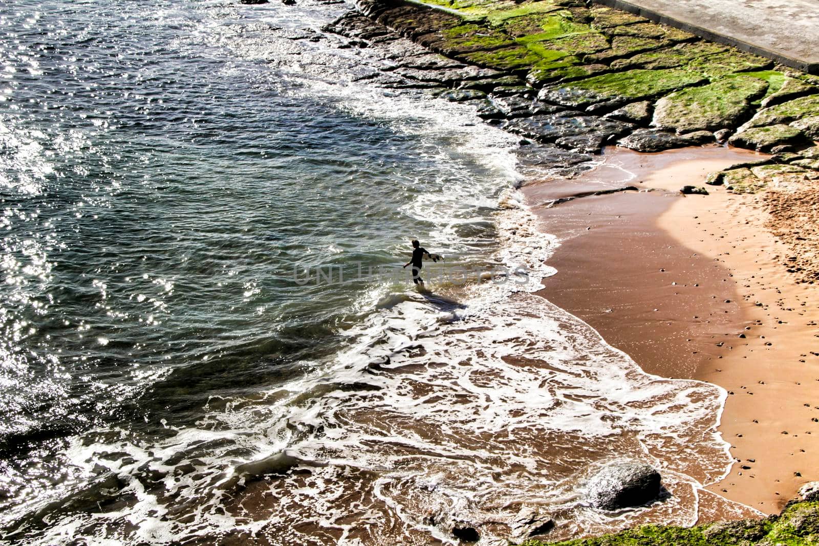 Surfer in the Beautiful Azarujinha beach with rock formations in Estoril, Lisbon, Portugal, in a sunny day of winter