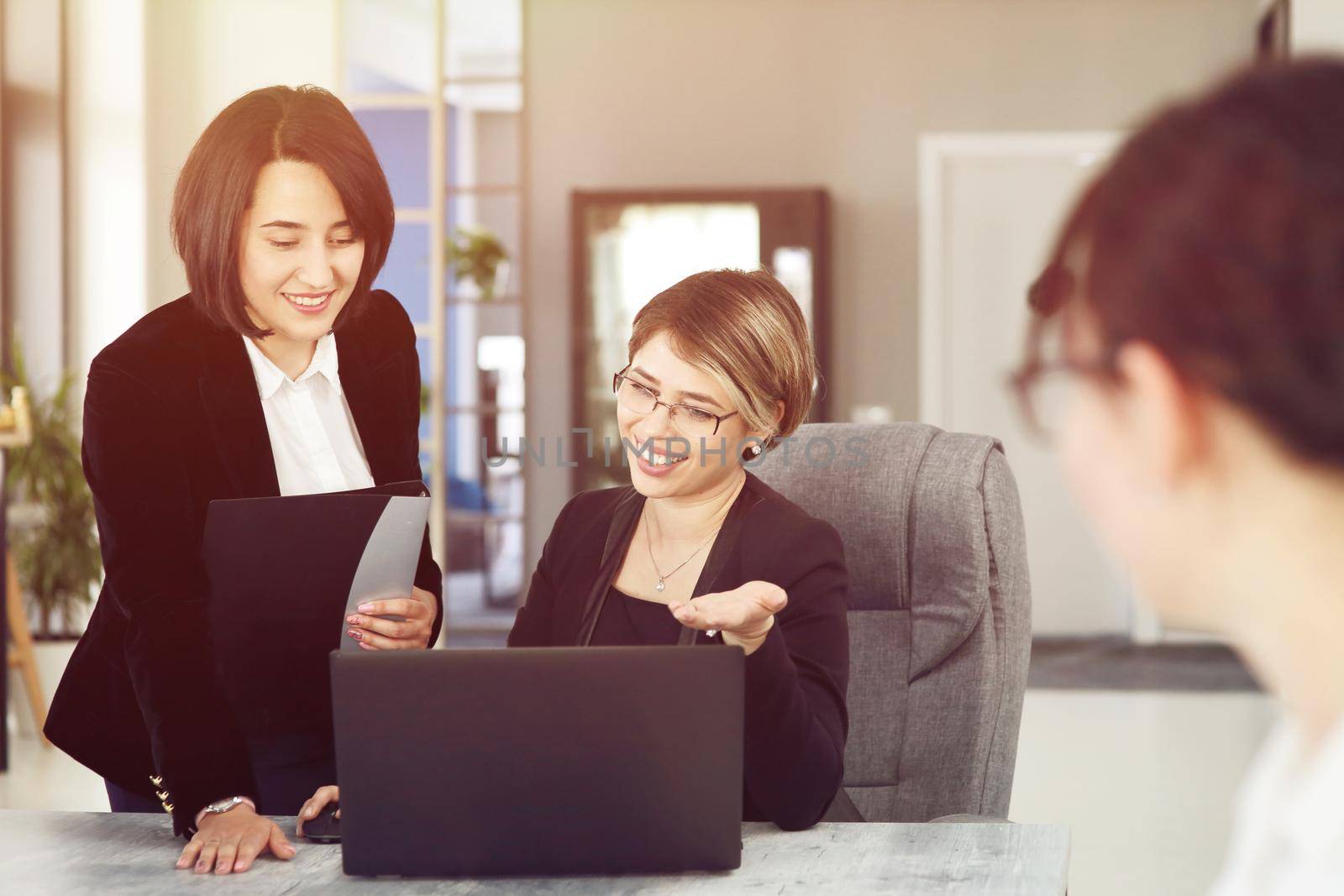 Two young business women in the office, analyzing information looking into a laptop and smiling by selinsmo