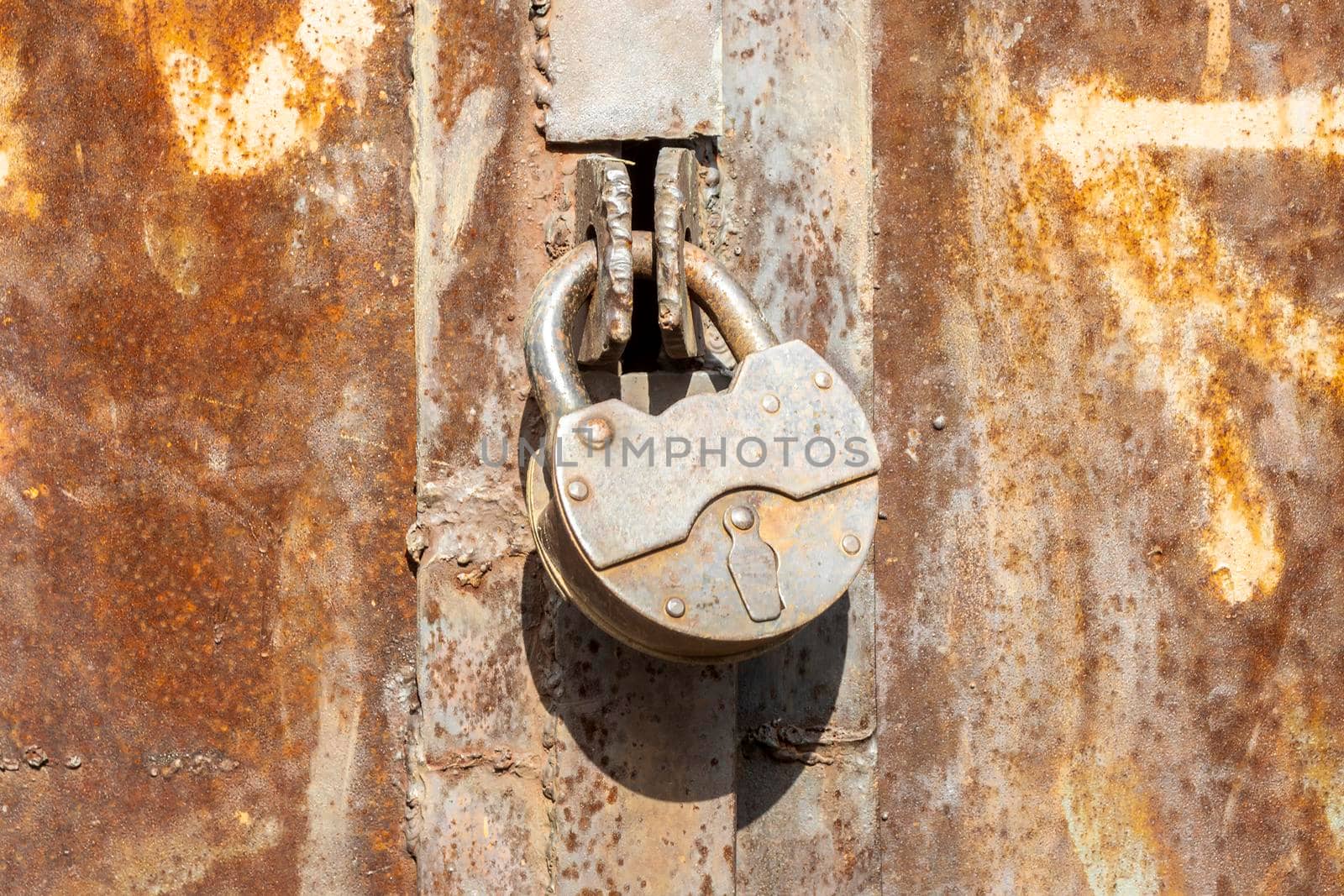 Iron lock on rusty doors. Sunny autumn day. Front view by Essffes