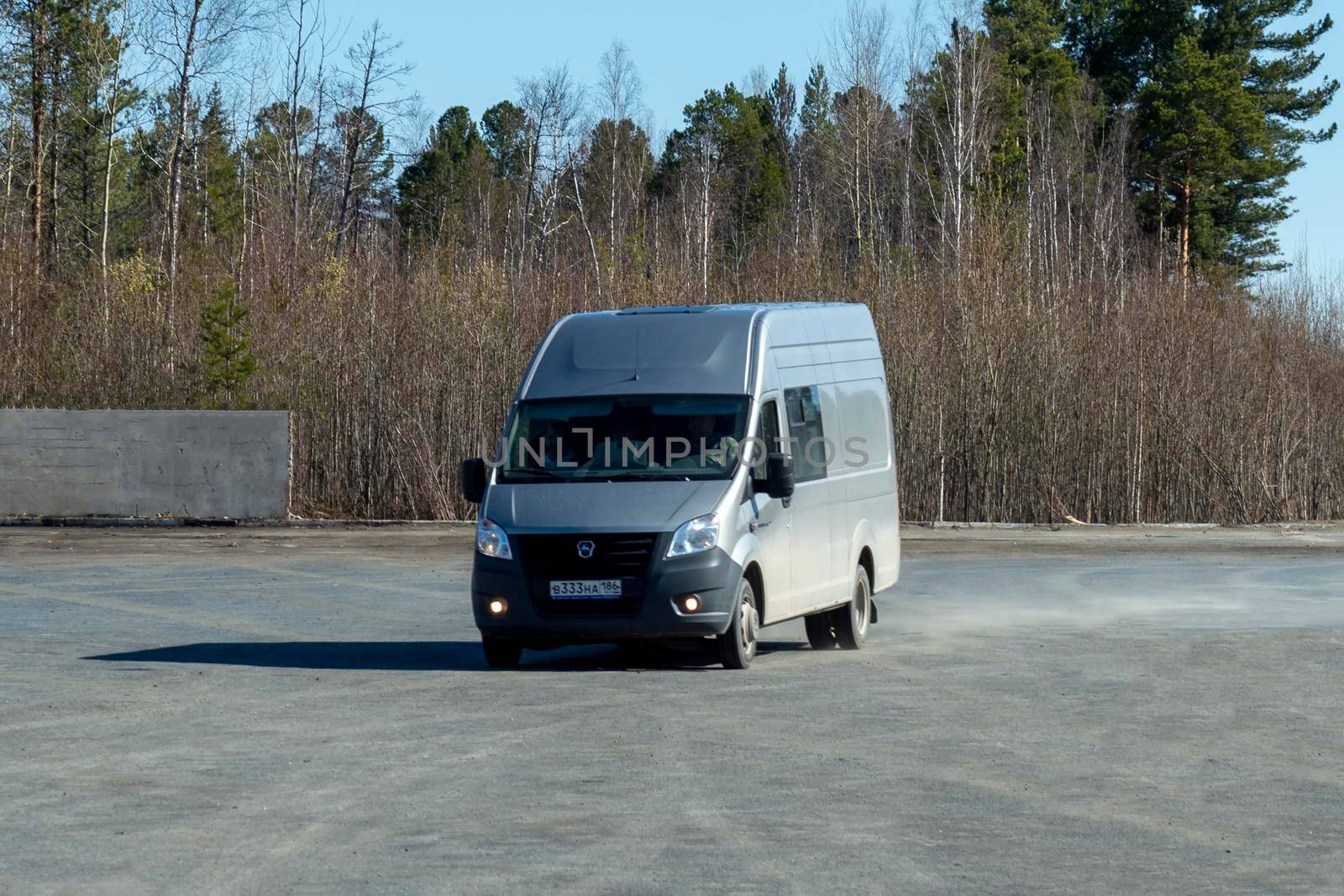A grey van enters a parking lot near road. Surgut, Russia - 16 April 2021 by Essffes
