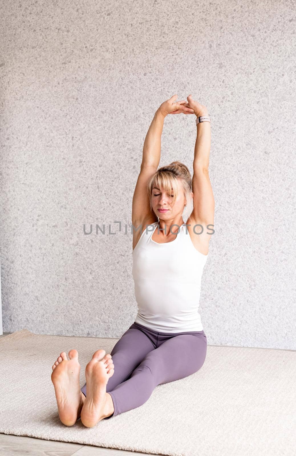 Blond woman practising yoga at home, stretching by Desperada