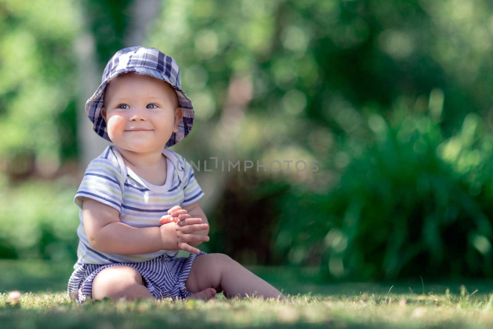 Cute baby sitting on the grass in the garden and applaud