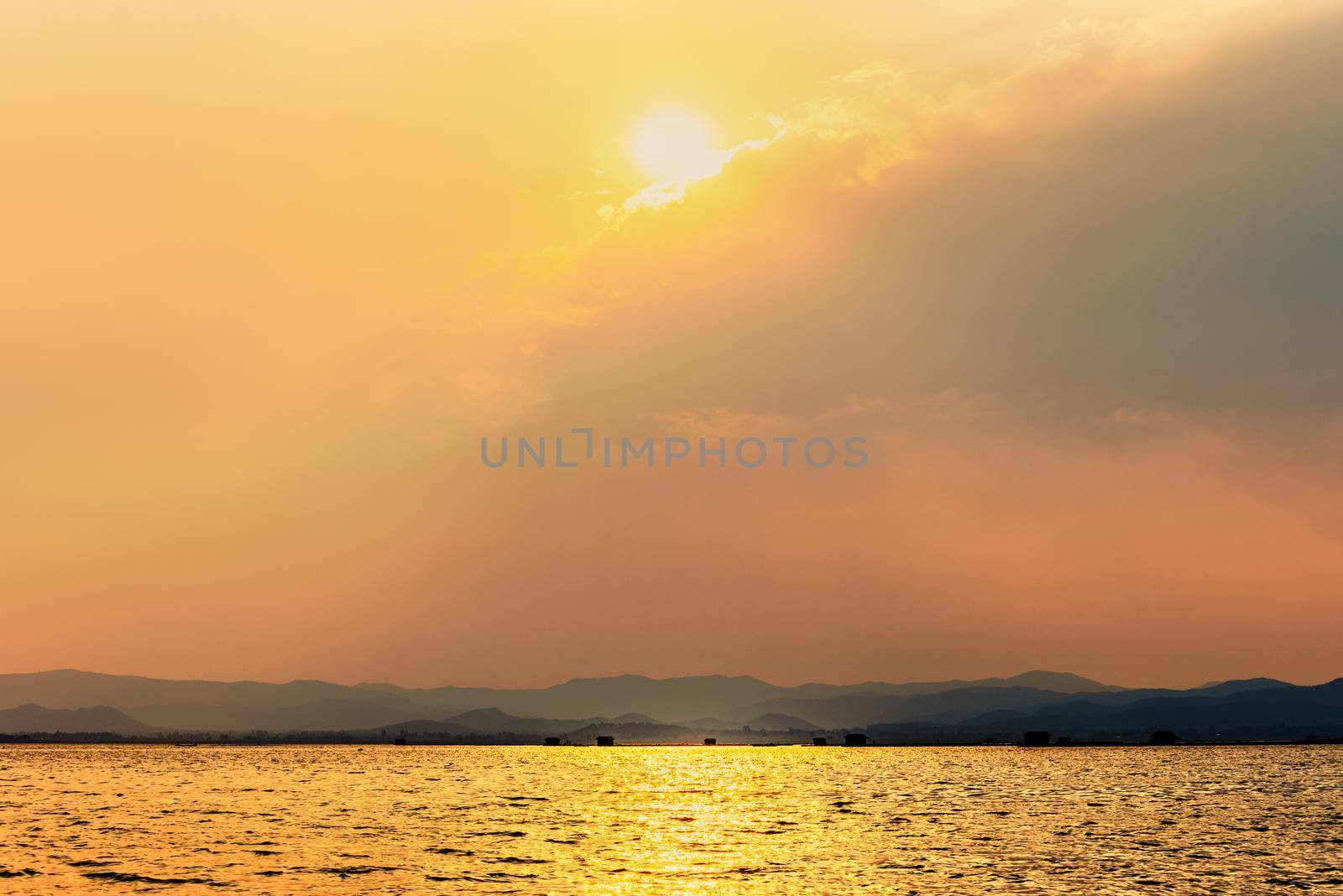 Beautiful nature landscape sun shines bright golden in the cloud reflect yellow light on the sky and water surface tropical lake in summer mountain background at Krasiao Dam, Suphan Buri, Thailand