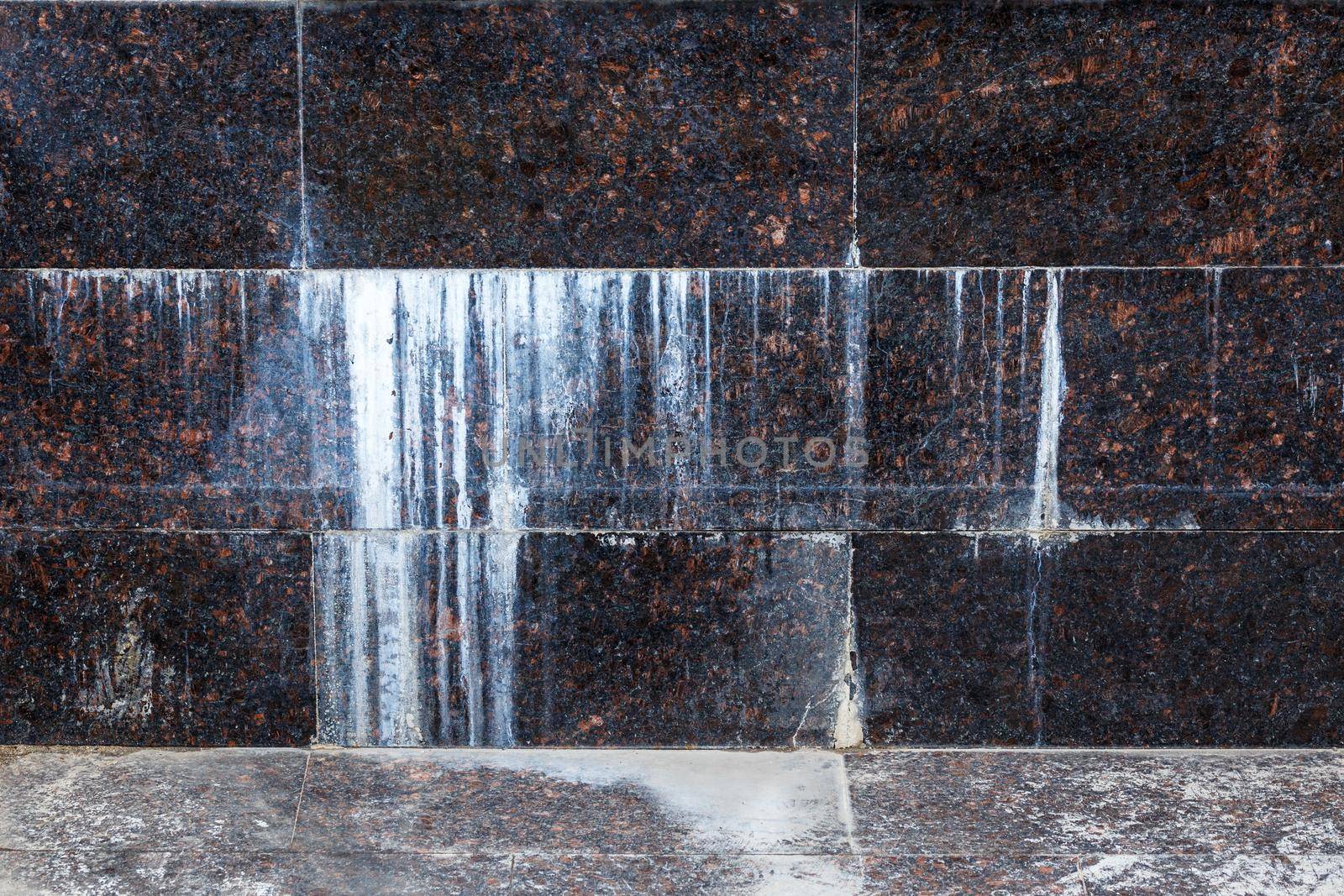 flat wall with rectangular natural tan brown granite tiles with white mineral drips.