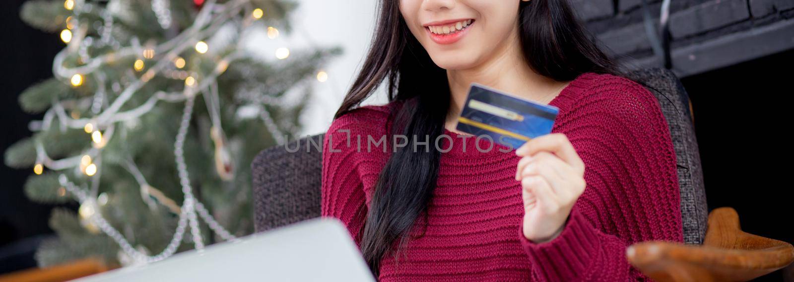 Young asian woman online shopping in Christmas with credit card on laptop computer, female buying and payment with debit card, xmas in holiday, happy new year, customer with purchase to internet. by nnudoo