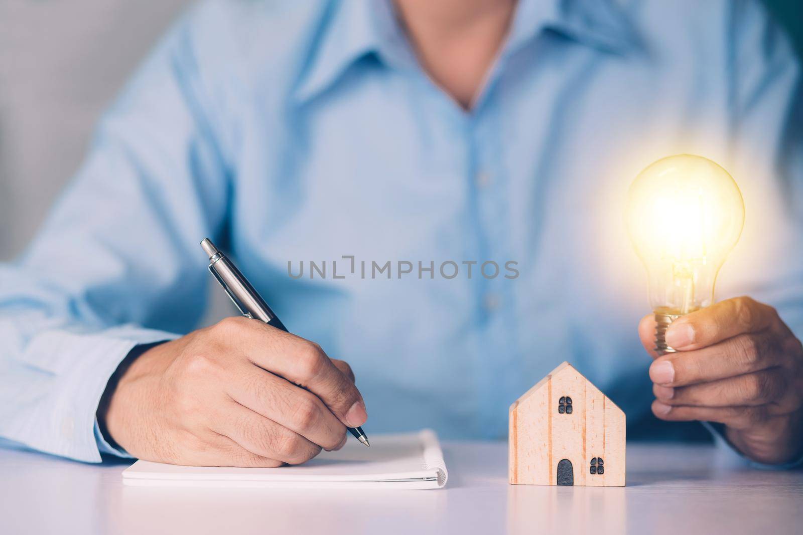 Businessman holding light bulb while home wooden for solution innovation and environment, thinking idea for planning buy house, residential with eco and saving energy, business and finance concept.