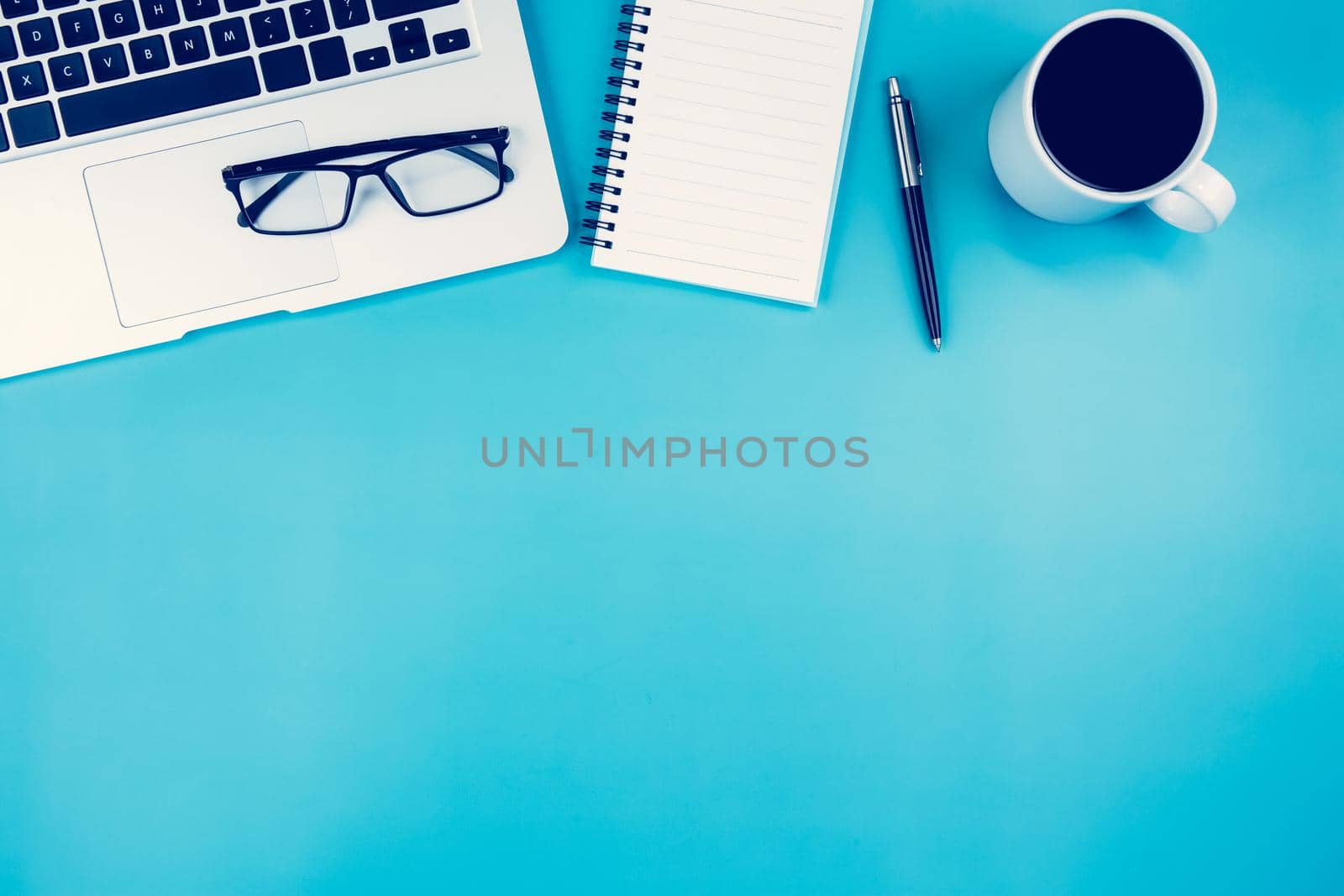 Flat lay of laptop computer and cup of coffee on desk in office, workplace and notebook and glasses and book on blue background, workspace and copy space, top view, business and communication concept. by nnudoo