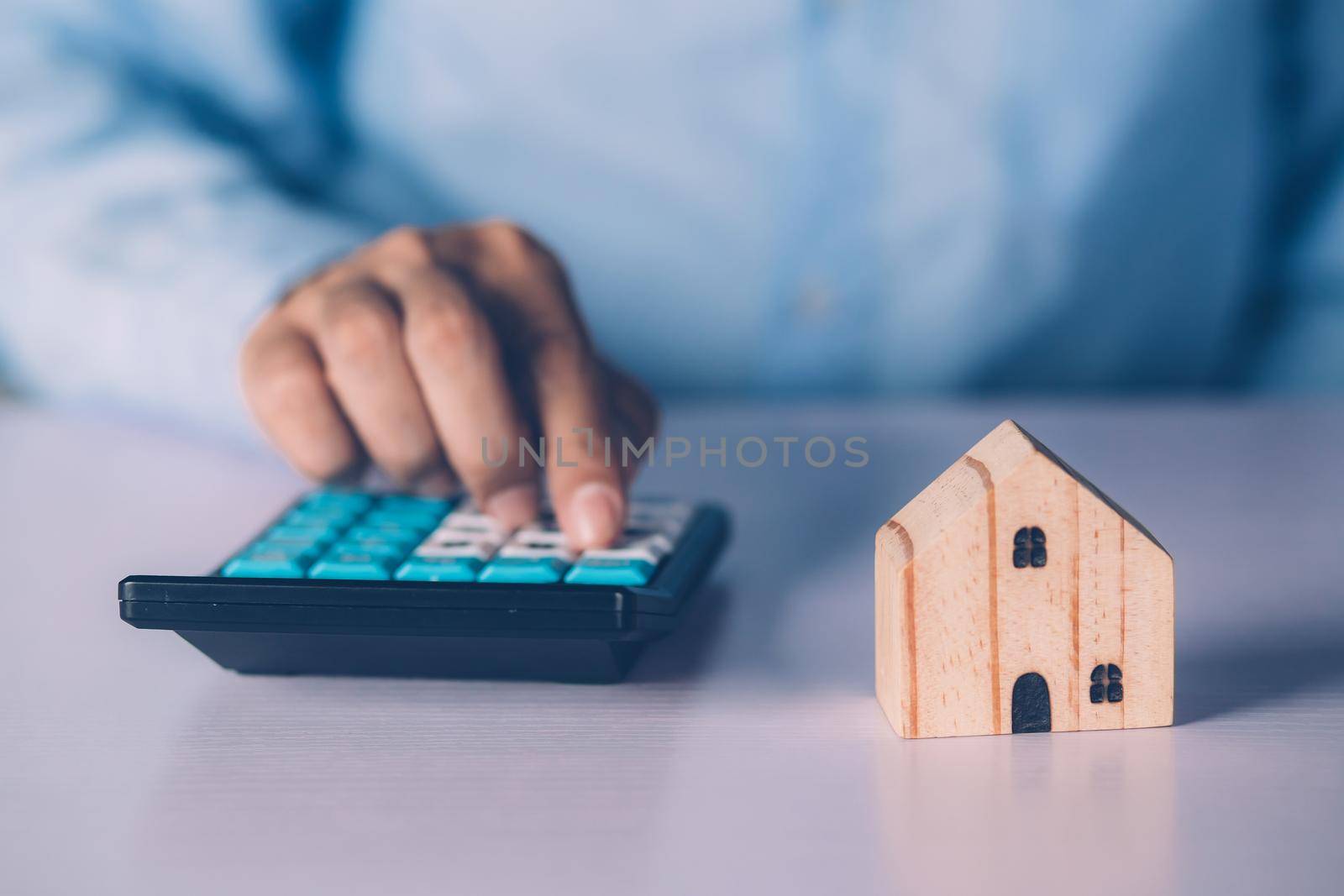 Hand of businessman planning and calculate expense and mortgage with calculator and home on desk, insurance and budget of residential, examining of loan and residence, business and property concept.