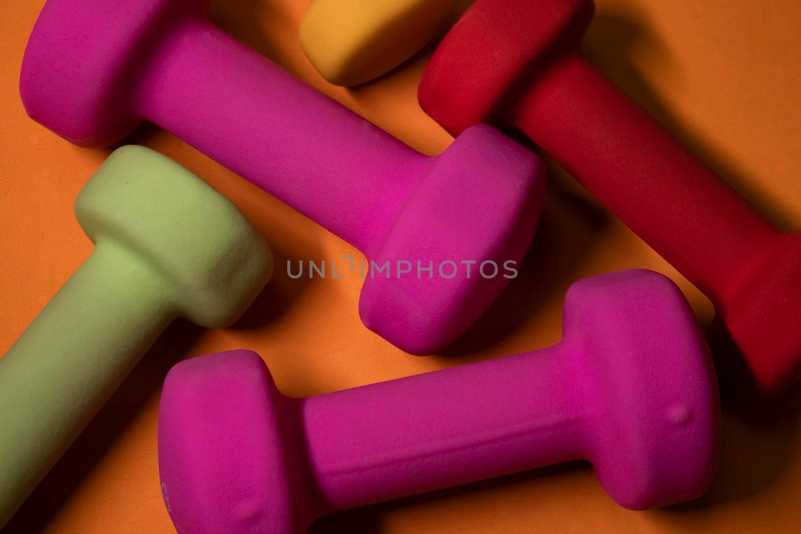 pink, green, red and yellow small dumbbells on orange background. Sport concept