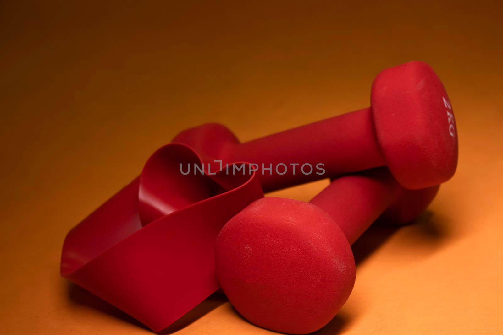 Bright red small dumbbells with fitness bands heart-shaped on an orange background. Sport concept. High quality photo