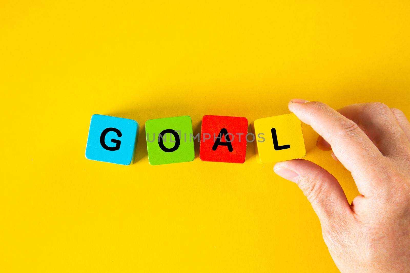 Man hand placing the wooden cubes with the word GOAL on yellow background. Business goal setting concept.