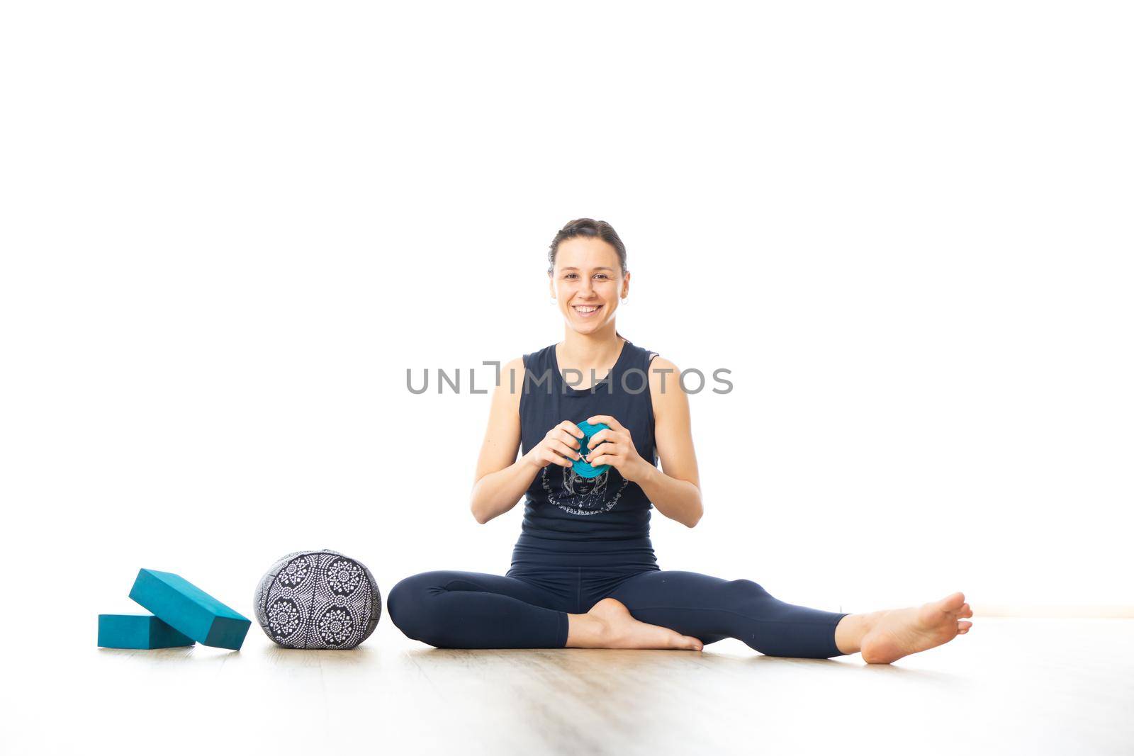 Restorative yoga with a bolster. Young sporty female yoga instructor in bright white yoga studio, smiling cheerfully while preparing restorative yoga exercise props.