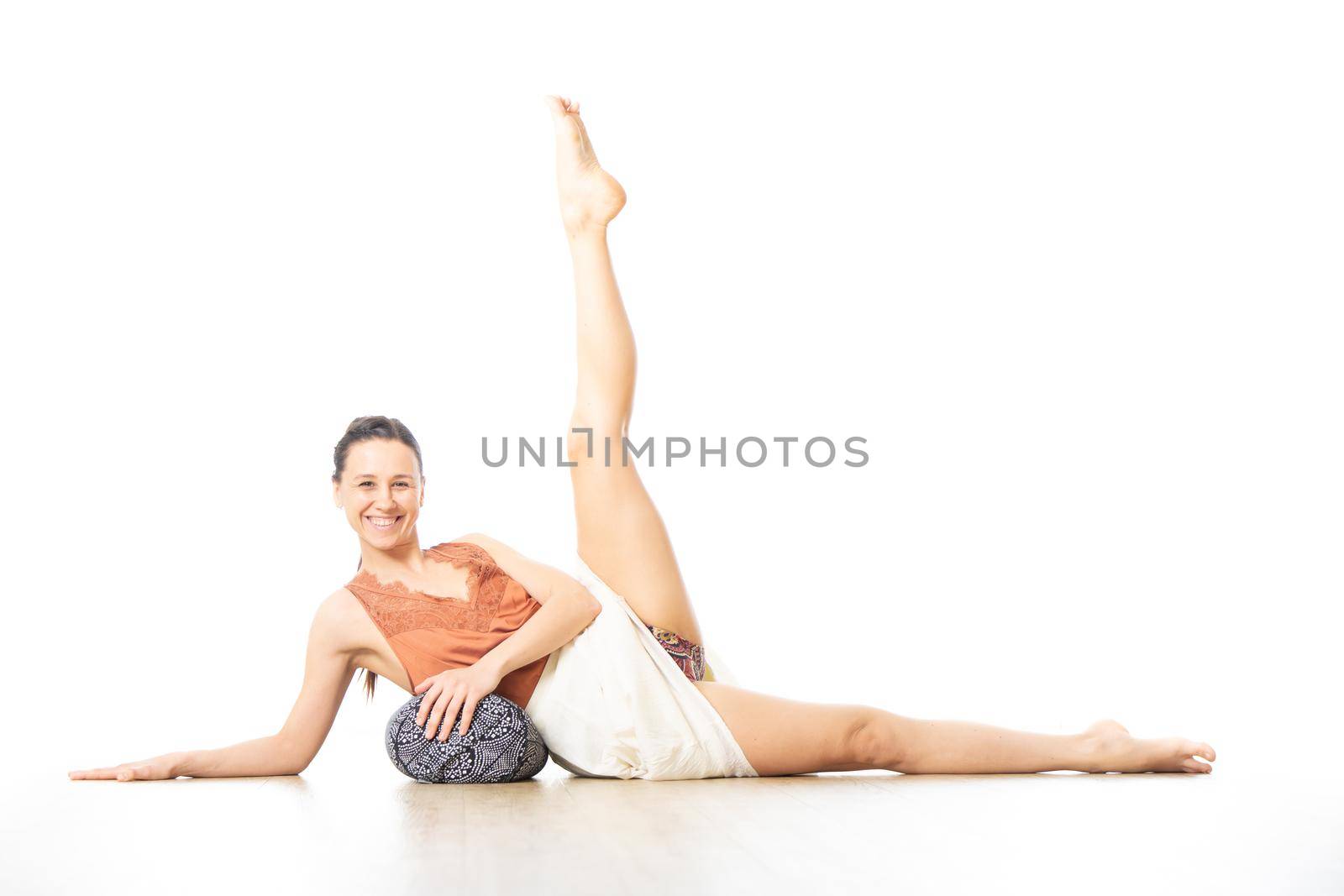 Young sporty healthy woman in bright white yoga studio, lying on bolster cushion, stretching, smilling, showing love and passion for bolster yoga. Healthy lifestyle concept.