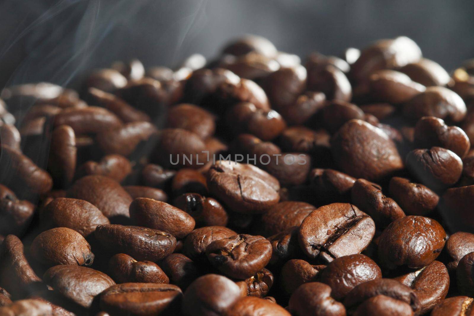 Hot roasted coffee beans and steam on black background with copy space