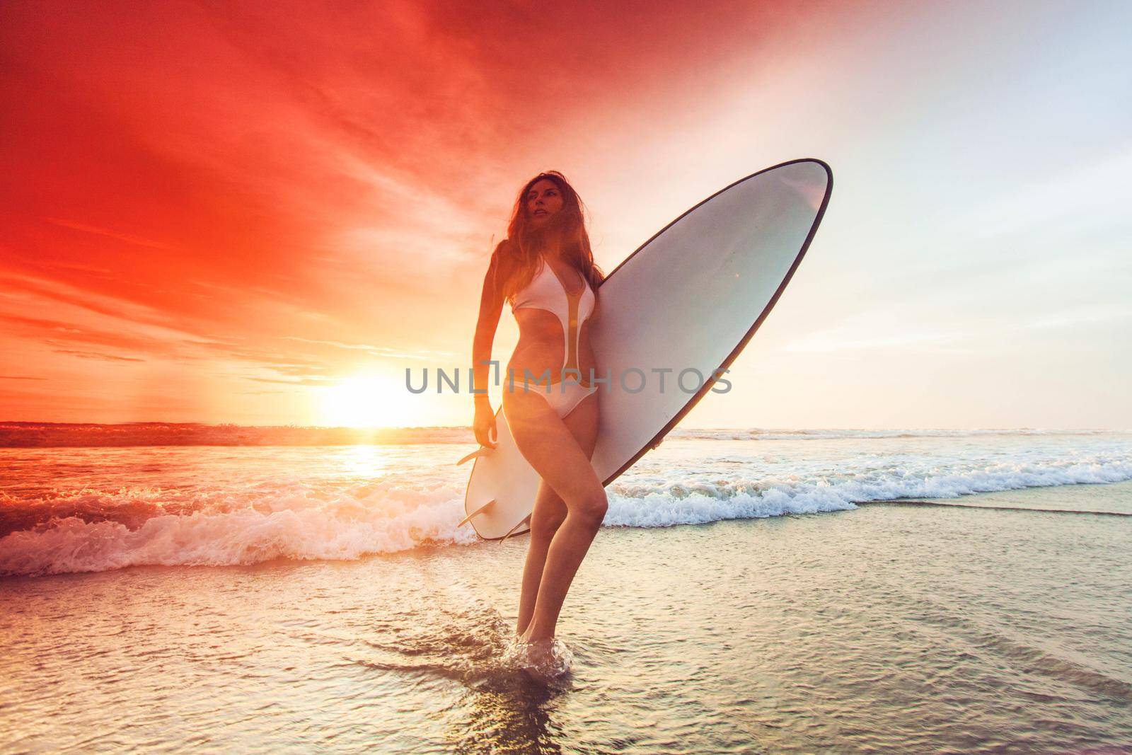 Woman holding surfboard at sunset by Yellowj
