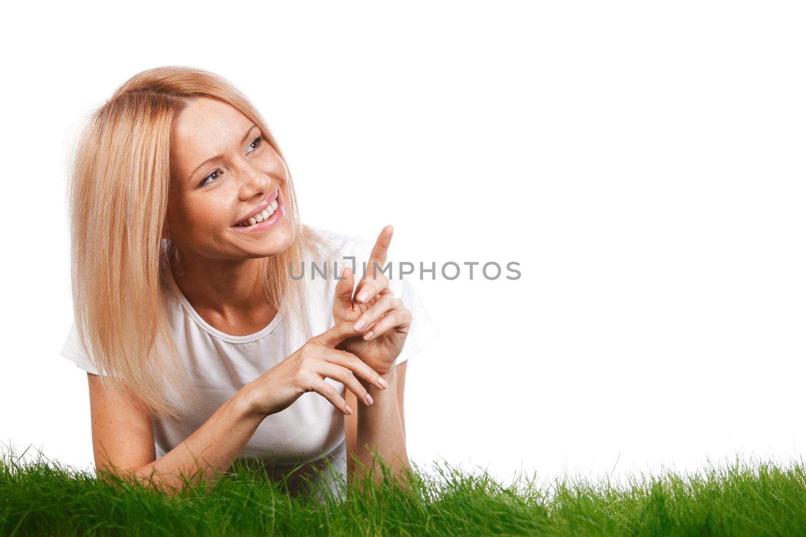 Beautiful young blonde smiling woman lying on grass, showing and presenting copy space, isolated on white background