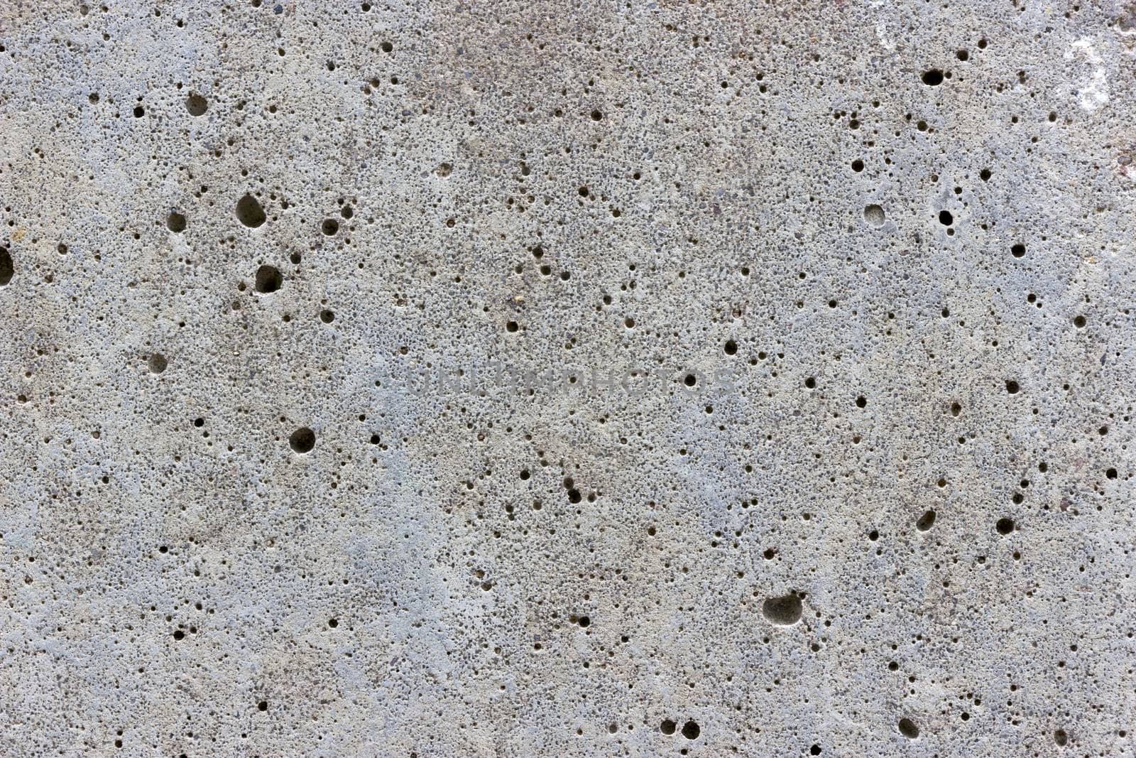 A flat grey concrete surface. The surface is textured and covered in holes from lots of tiny air bubbles.