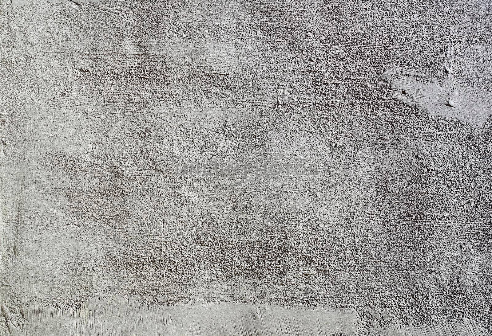 The heavy surface texture of an external wall covered in white plaster.