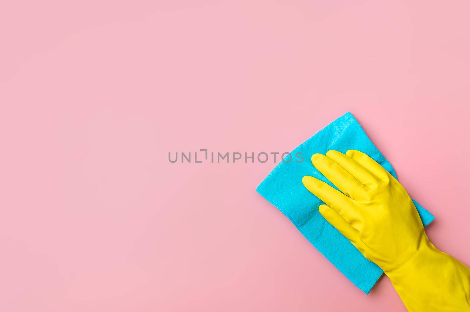 Employee hand in yellow rubber protective glove hold blue rag wiping pink wall background. House cleaning service, general or regular cleanup concept. Empty place for text or design