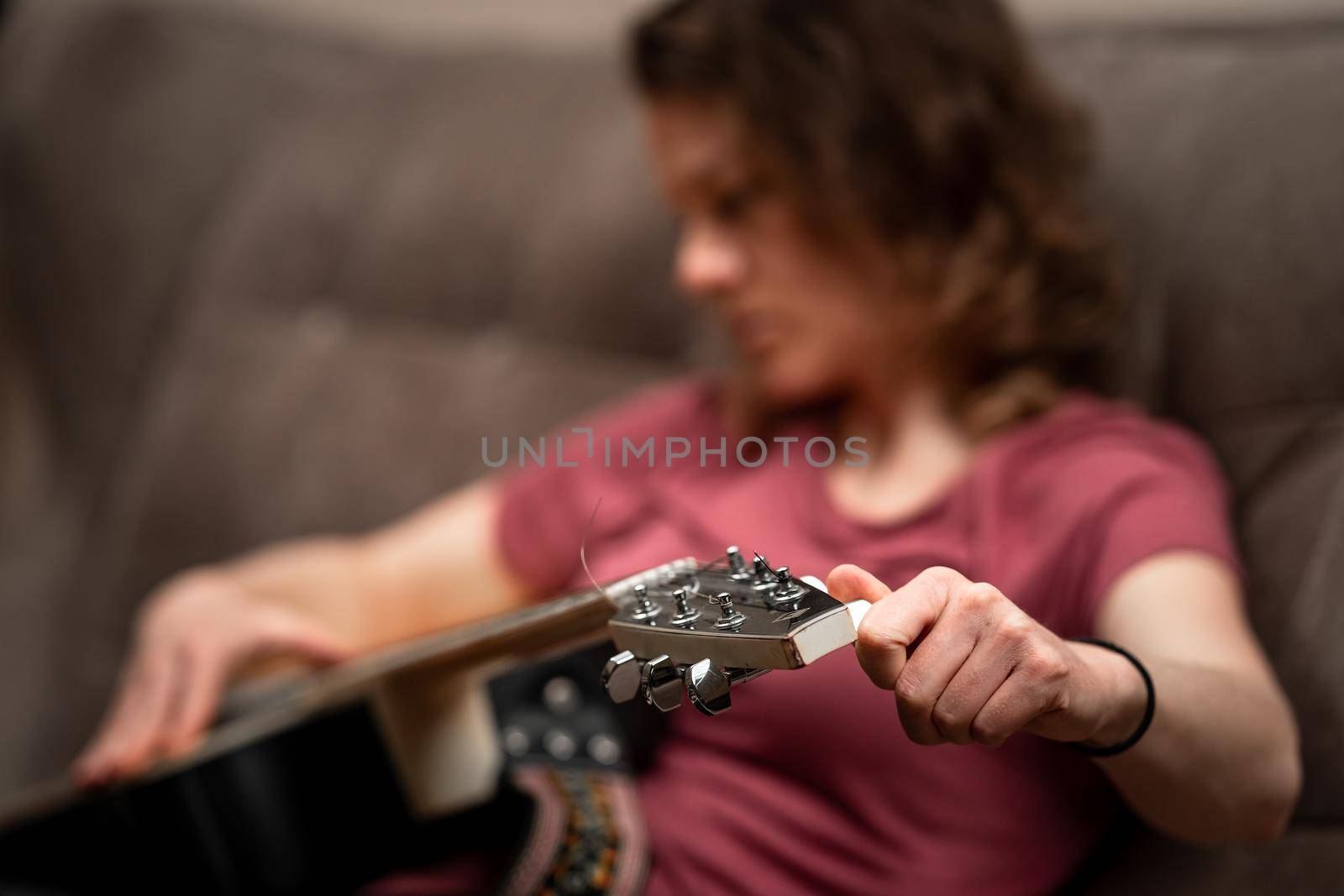 woman tuning guitar at home on the couch.