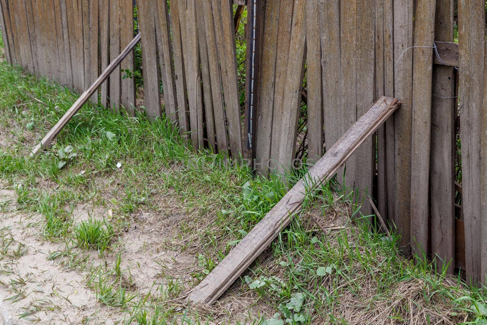 old dusty rickety wooden fence with plank props and grass close up with selective focus.