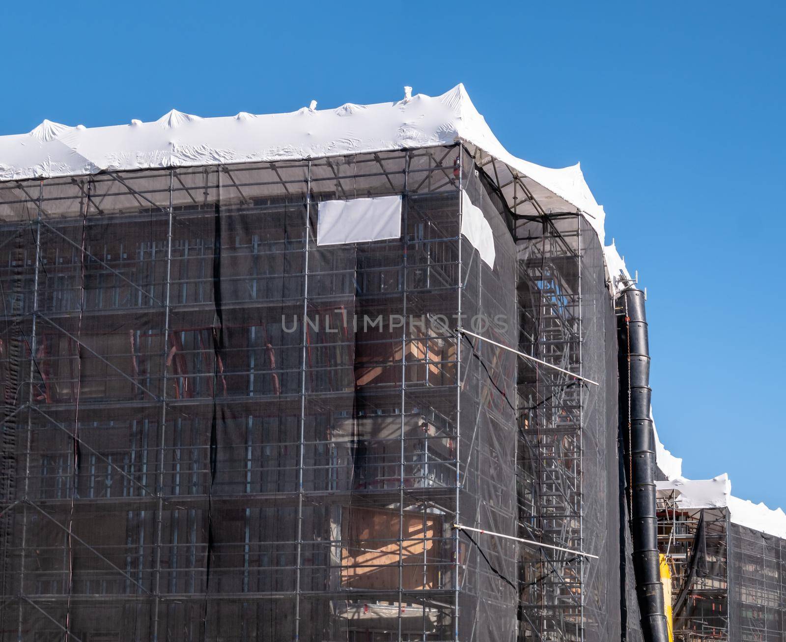 Office building under construction on blue sky background. scaffoldings wrapped into the net on a construction site