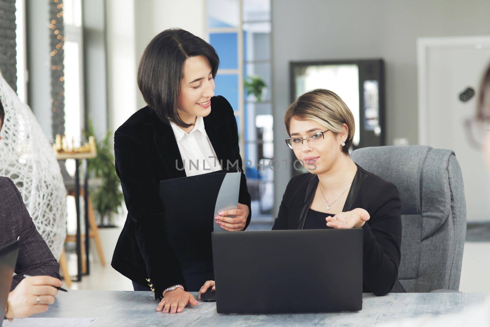 Two young business women in the office, analyzing information looking into a laptop, and smiling. 
