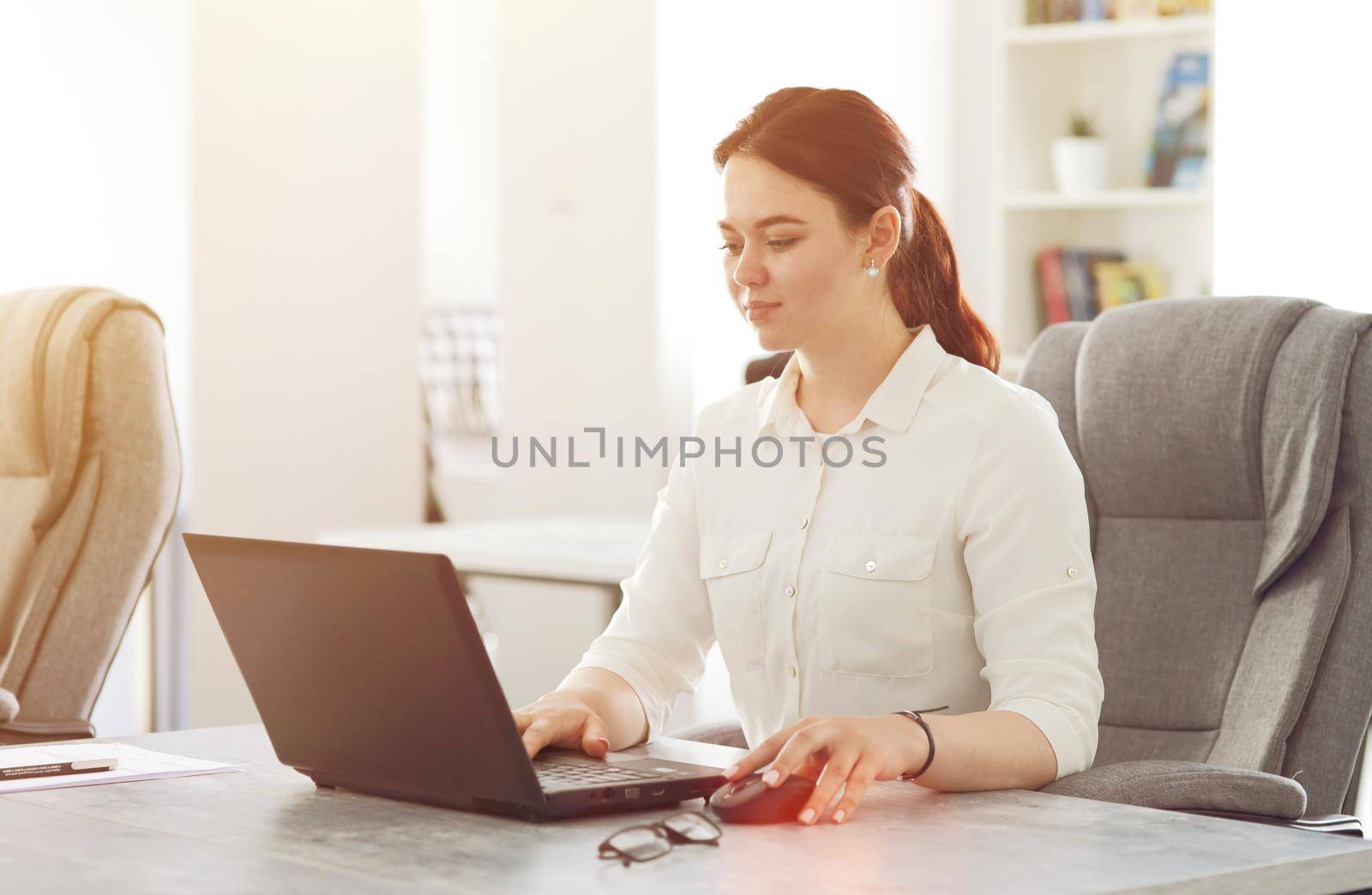 Young attractive business woman working in office smiling looking into laptop by selinsmo