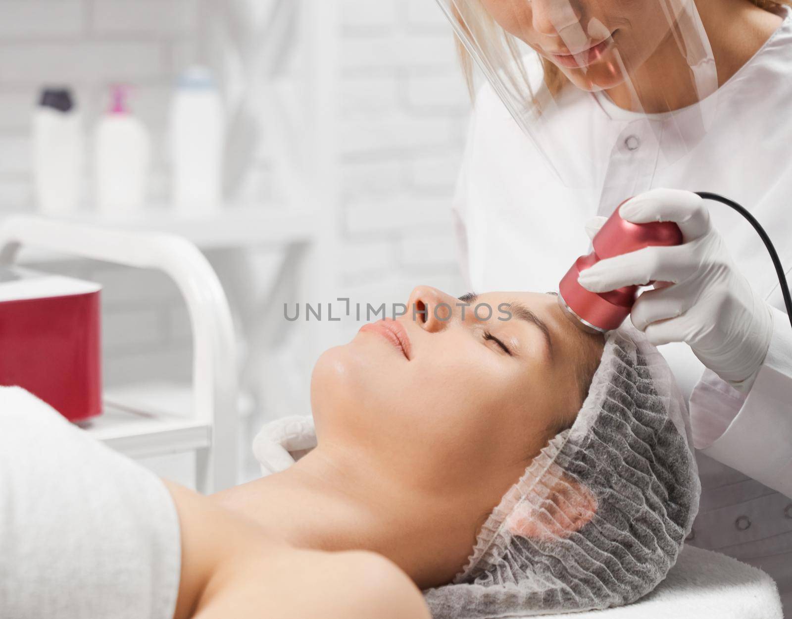 Side view of young beautiful woman lying on procedure cleaning face with special modern professional equipments. Concept of improvements condition skin with special cosmetics.