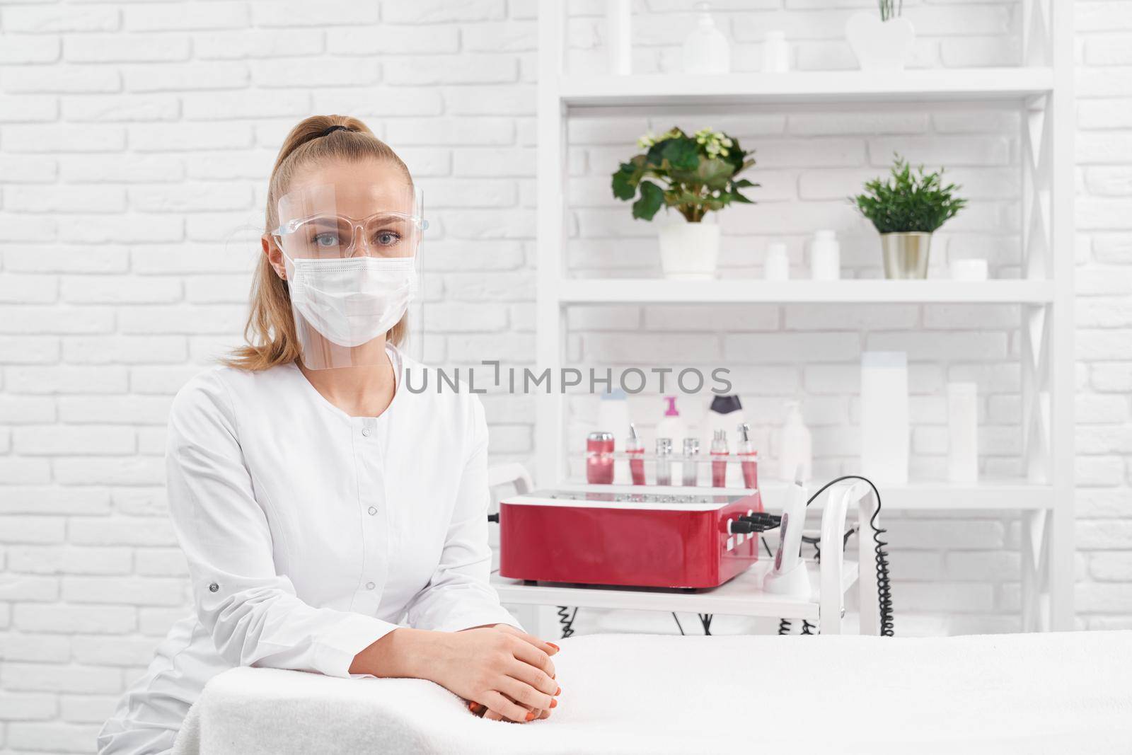 Close up portrait of young beautician in protective mask and special face shield waiting for clients. Concept of preparing for procedures with modern professional equipments in salon. 