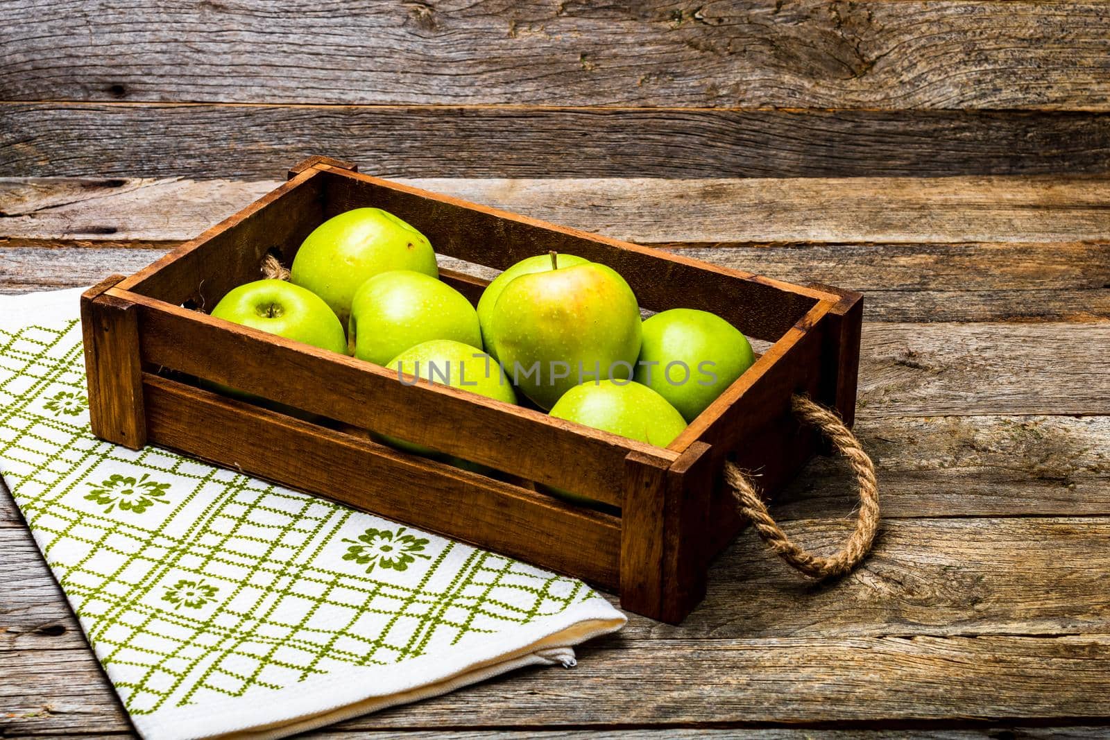 Wooden crate with ripe green apples on wooden table.