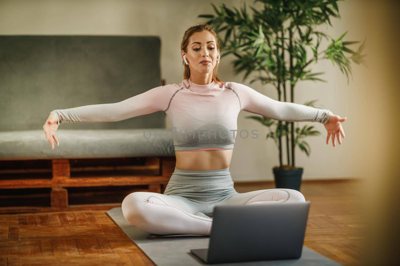 An attractive young woman using laptop to record her vlog about healthy living while practicing yoga inside of a studio.