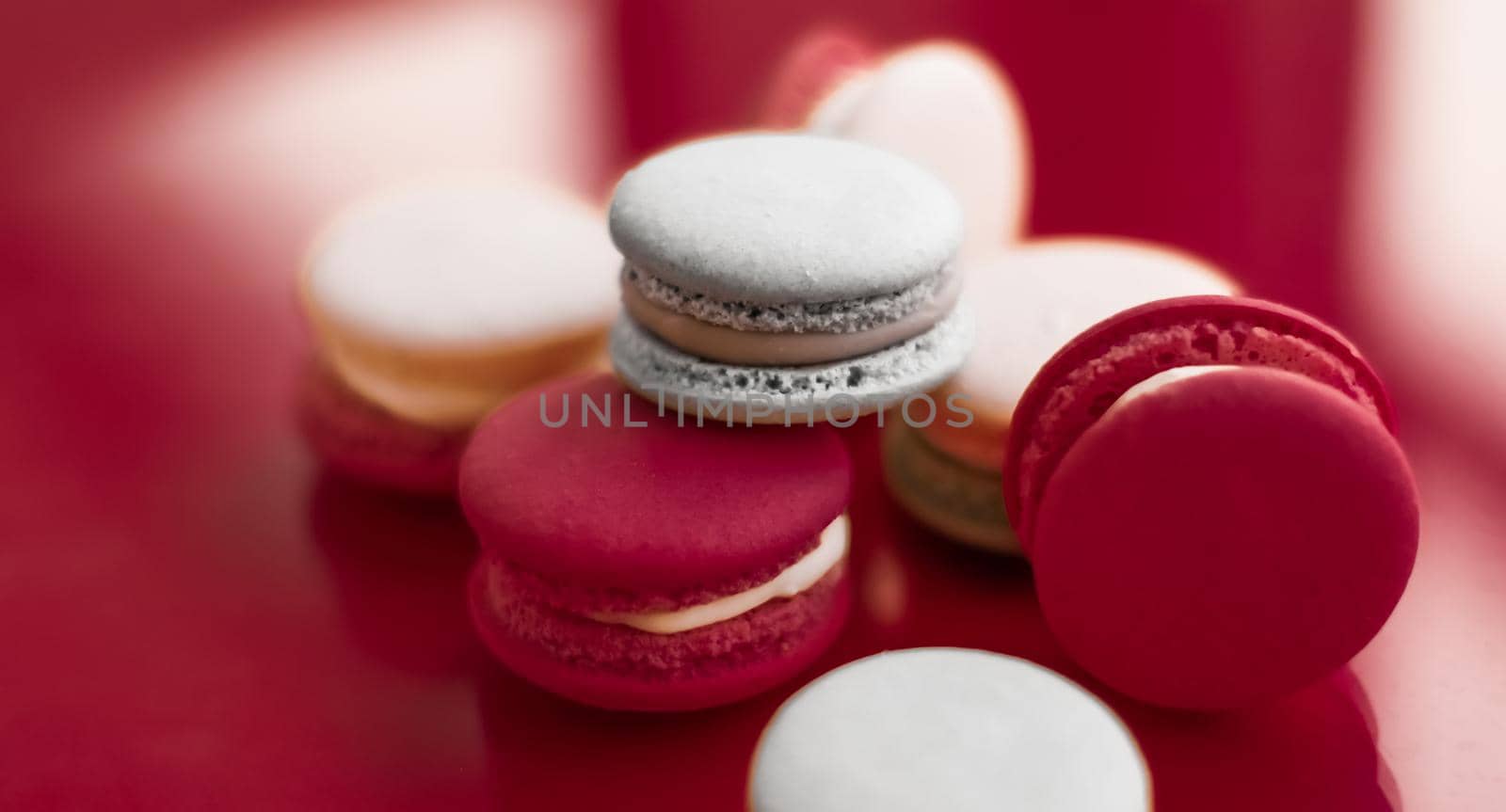 Pastry, bakery and branding concept - French macaroons on wine red background, parisian chic cafe dessert, sweet food and cake macaron for luxury confectionery brand, holiday backdrop design